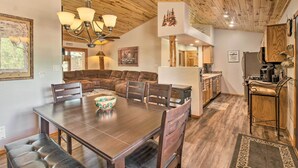 A spacious living area with a large wooden dining table, comfortable seating, and a kitchen area with wooden cabinets and a bar. - 3 Mi to Trails: Woodsy Retreat in Overgaard! (Overgaard)