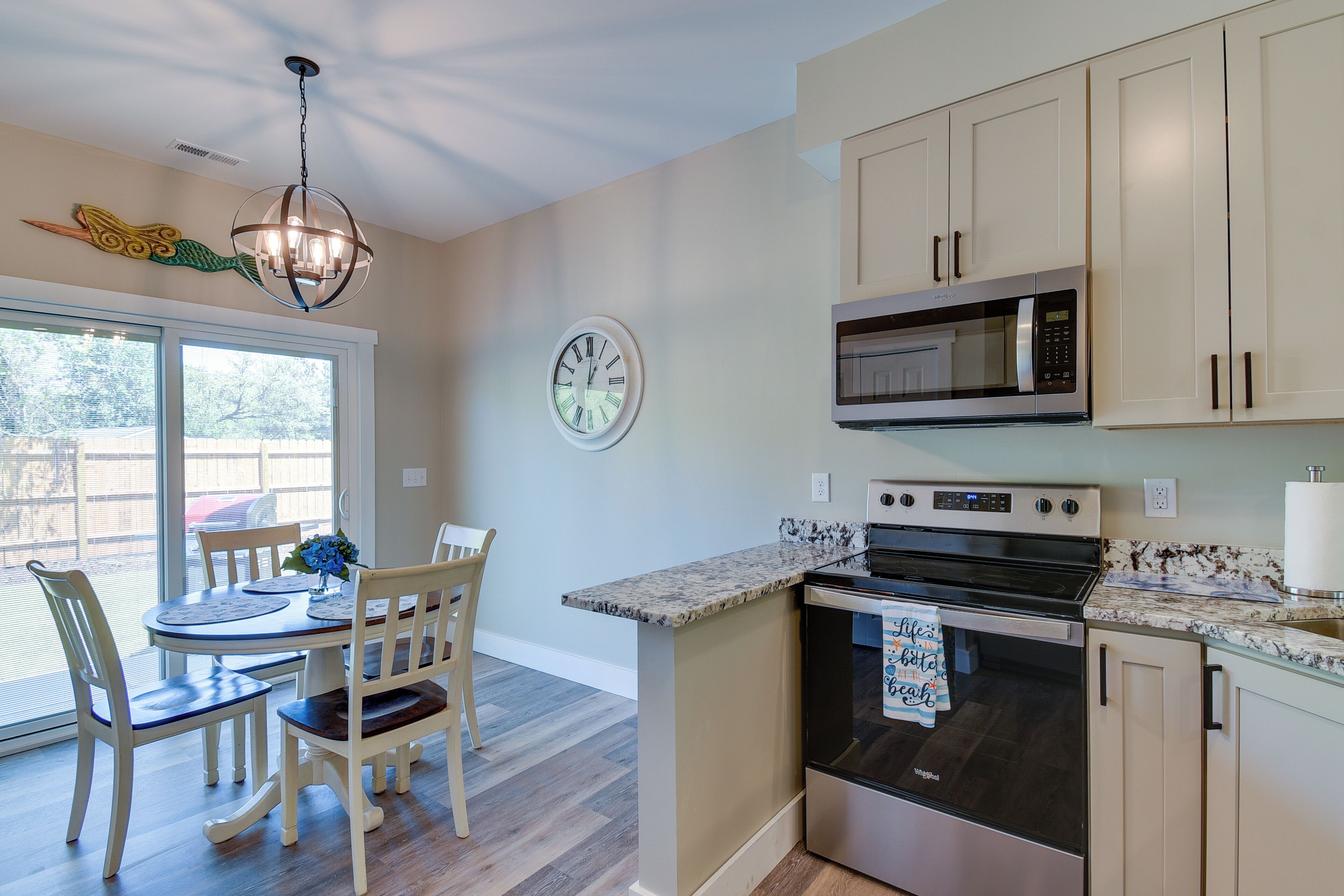 A kitchen with a dining area, featuring a chandelier, a clock, and a microwave.
