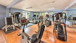Un gimnasio con diversas máquinas de ejercicio, un espejo grande y suelo de madera.