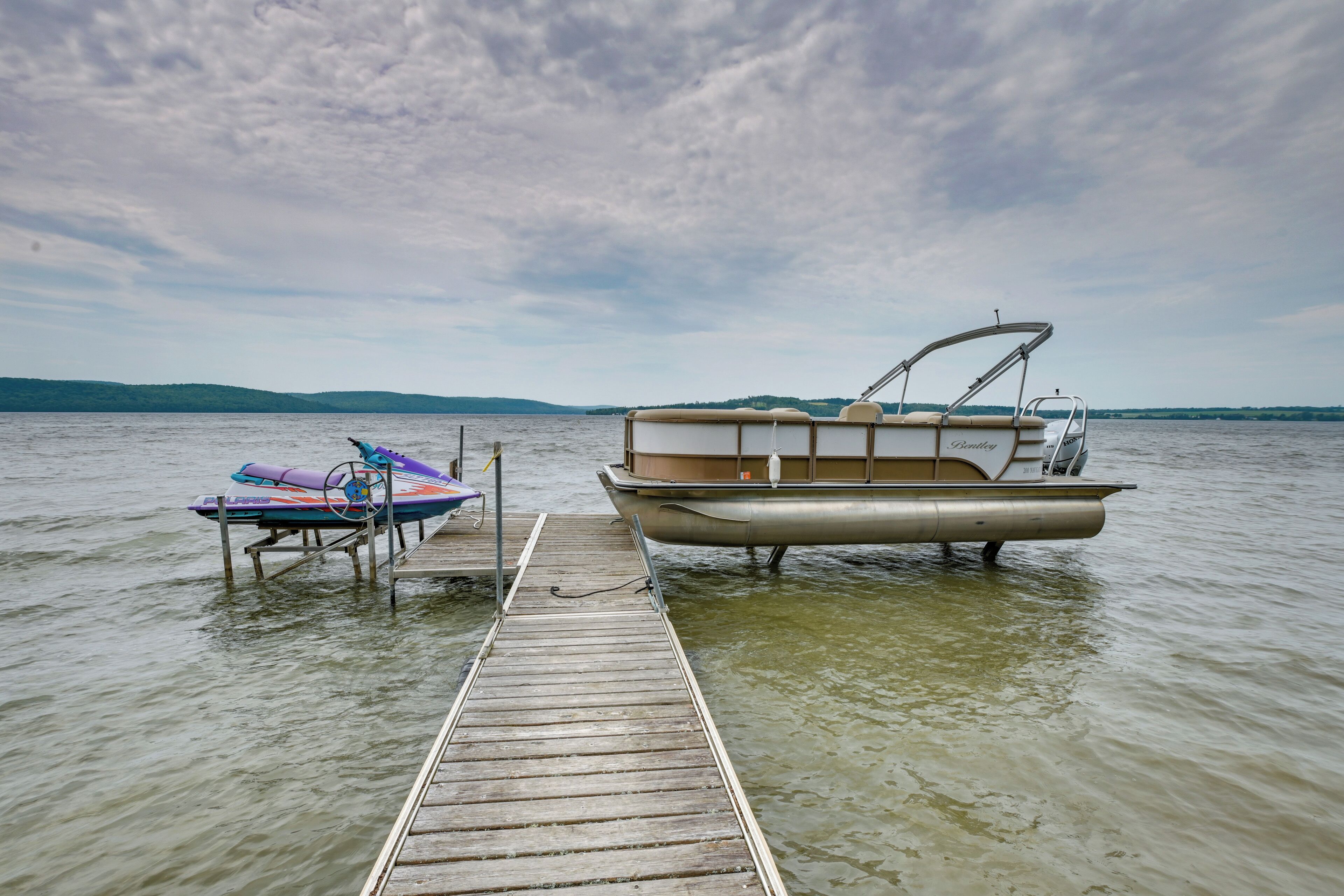 A wooden dock extending into calm water with a boat and a kayak docked at the end.