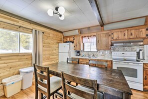 A kitchen with wooden cabinets, a large dining table, and a refrigerator. - Cozy Maine Lakefront Cabin Rental (Saint David)