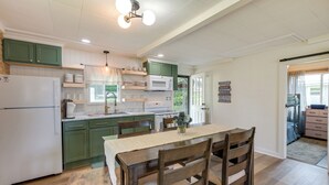 Eine Küche mit grünen Schränken, einem weißen Kühlschrank und einem Essbereich mit einem Holztisch und Stühlen.