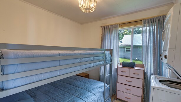 Ein Stockbett mit Schreibtisch und Schubladen, ein Fenster mit Vorhängen sowie eine Deckenleuchte.