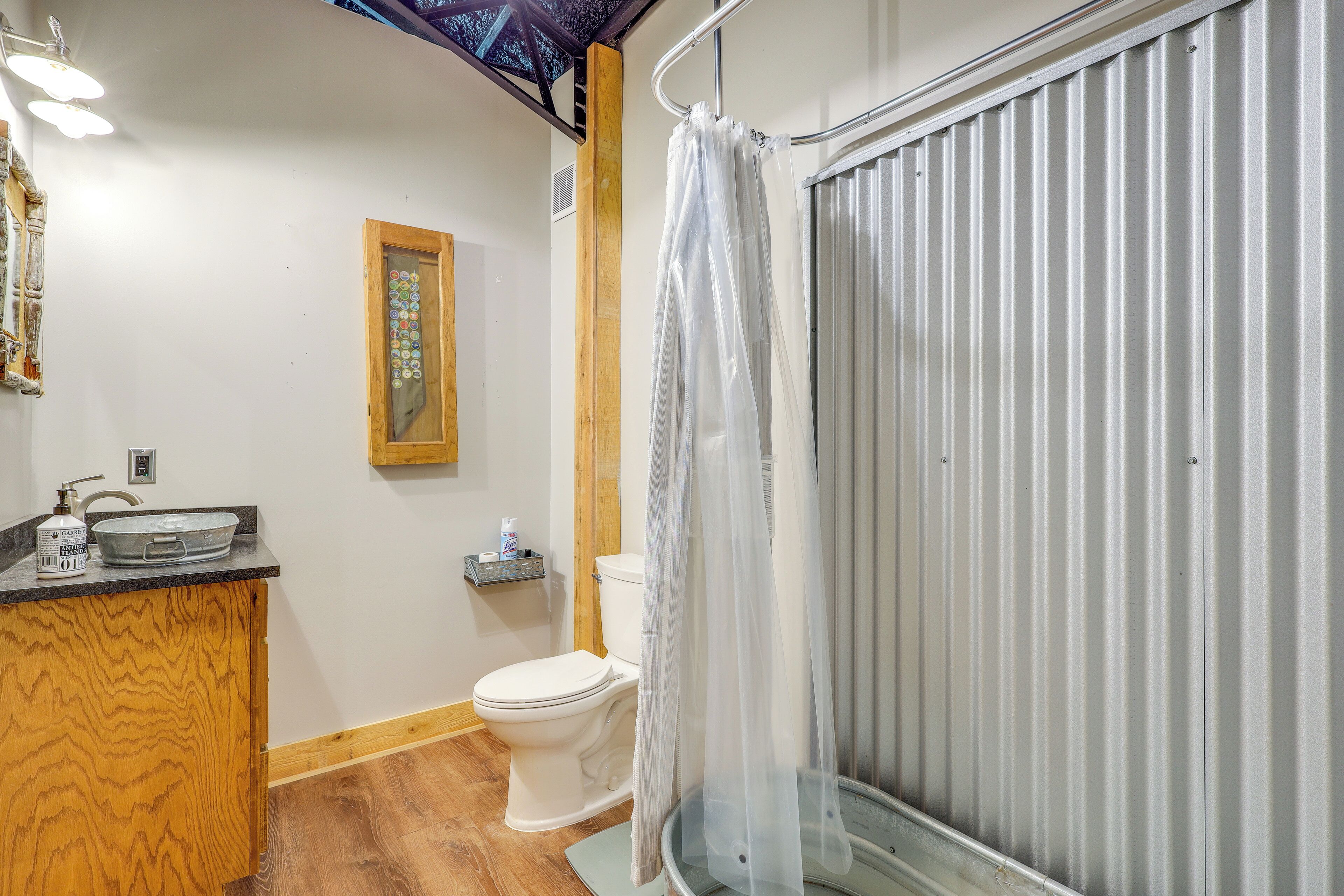 A bathroom with a wooden vanity, a toilet, a shower with a glass door, and a small shelf with toiletries.