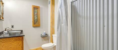 A bathroom with a wooden vanity, a toilet, a shower with a glass door, and a small shelf with toiletries.