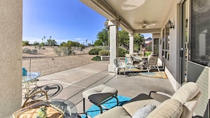A covered patio with outdoor furniture, a glass table, and a view of a fenced area with trees.