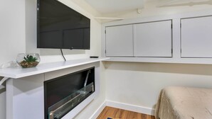 Quarto moderno com TV de tela plana fixada em uma prateleira branca, lareira embutida e cama com manta bege.
