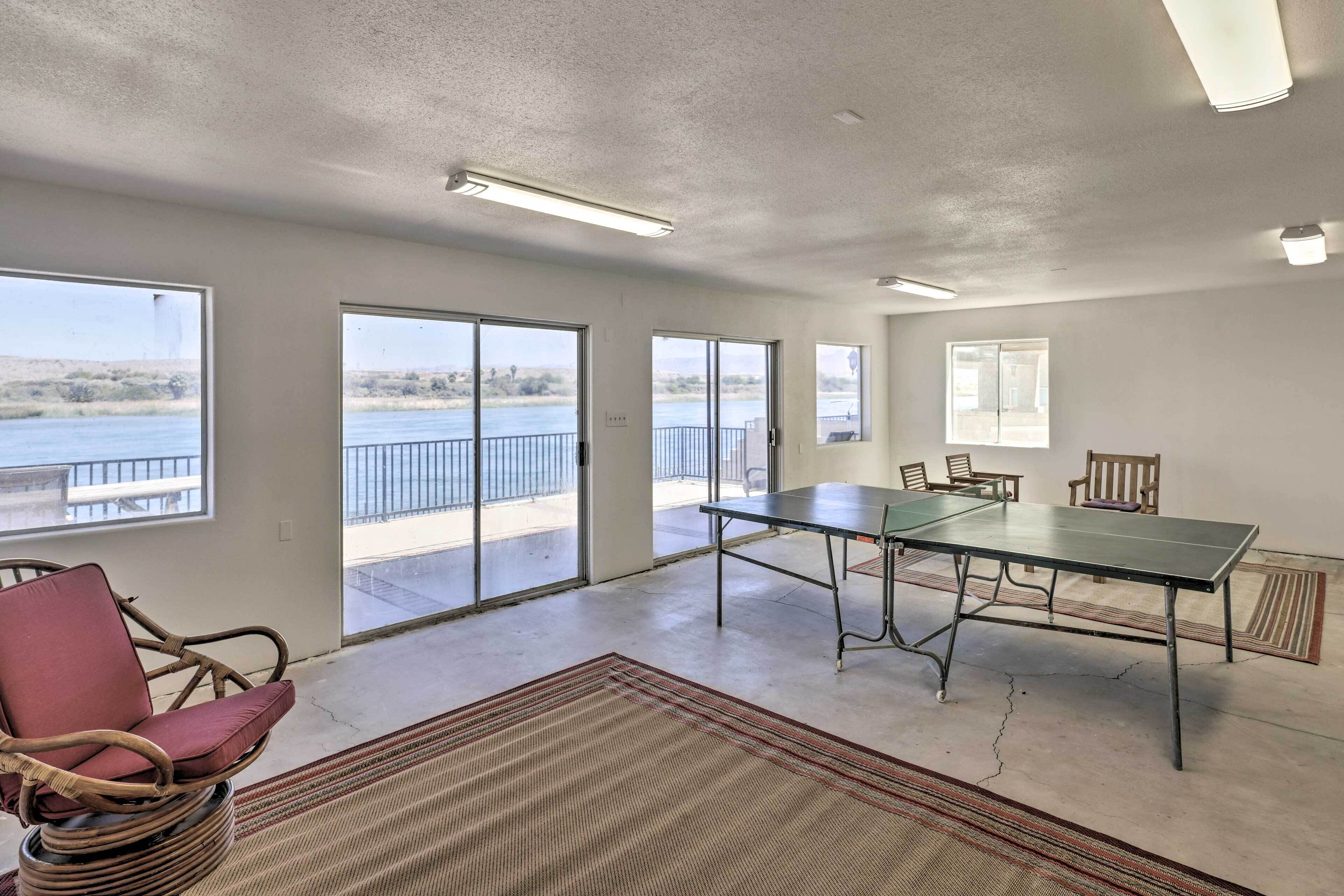 A spacious room with a large table and chairs, large windows with a view of a body of water, and a balcony with a railing.