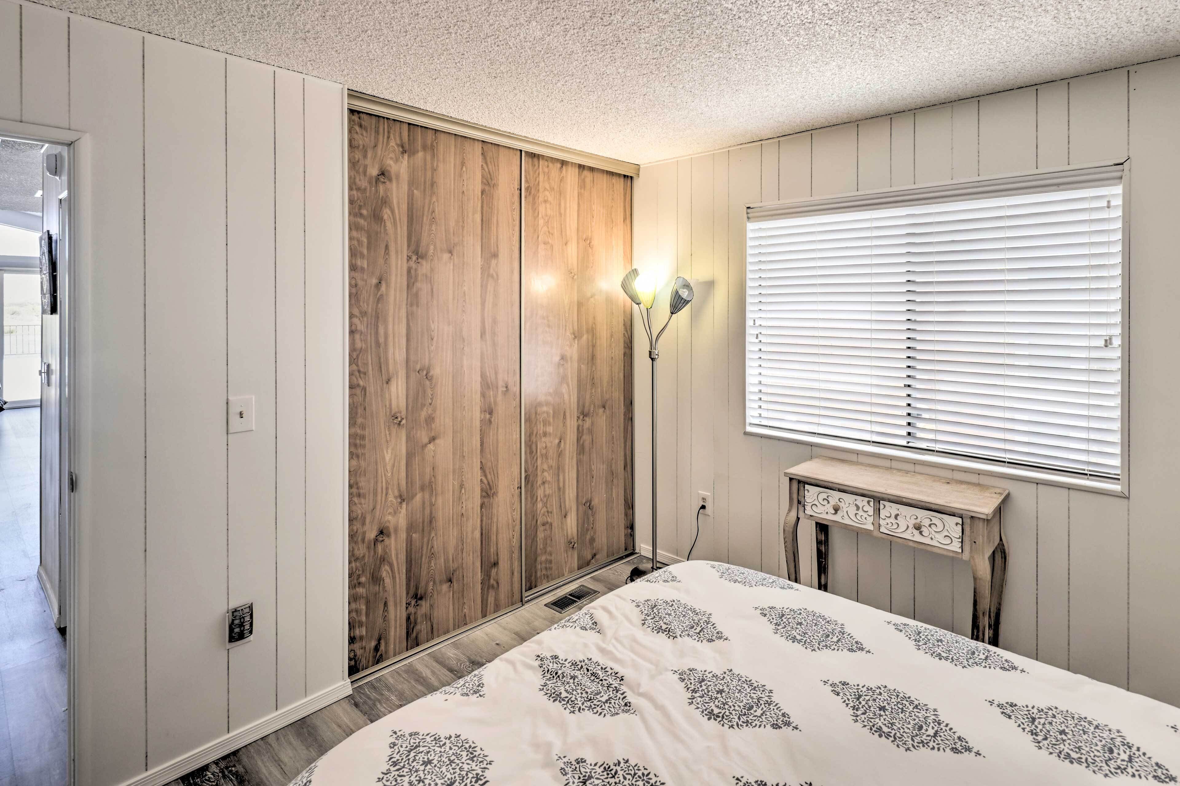 Een slaapkamer met een bed, een houten kledingkast, een wandlamp en een raam met jaloezieën.