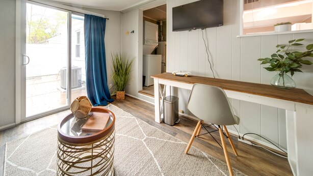 A compact living space with a kitchenette, a dining area with a wooden table and bar stools, a TV mounted on the wall, and a sliding glass door leading to an outdoor area. - Pet-friendly Mayfield Heights Vacation Rental! (Mayfield Heights)