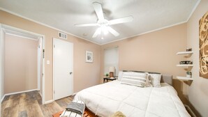 A bedroom with a bed, a ceiling fan, a nightstand, a window with blinds, and a door. - Pet-friendly Mayfield Heights Vacation Rental! (Mayfield Heights)
