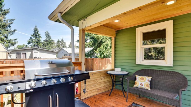 Une terrasse extérieure couverte, équipée d’un barbecue, d’un canapé en osier et d’une petite table.