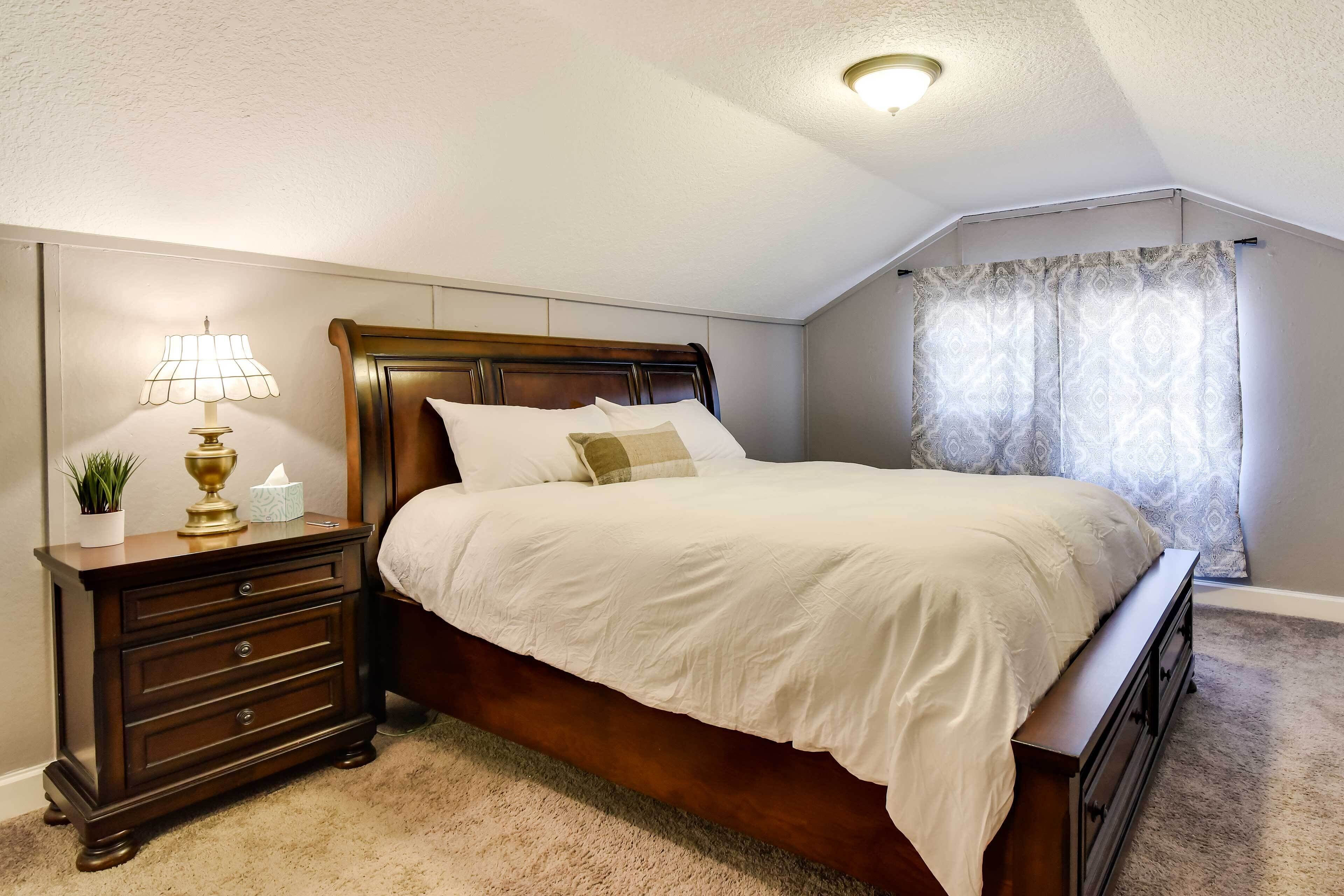 A bedroom with a wooden bed, a nightstand with a lamp, and a window with curtains.