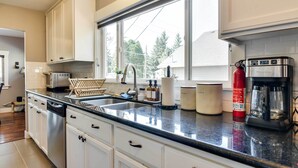 Une cuisine moderne avec des meubles blancs, une grande fenêtre, des appareils en acier inoxydable et une machine à café.