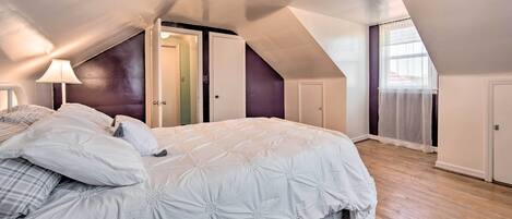 A bedroom with a large bed, a nightstand, a lamp, and a door leading to another room.