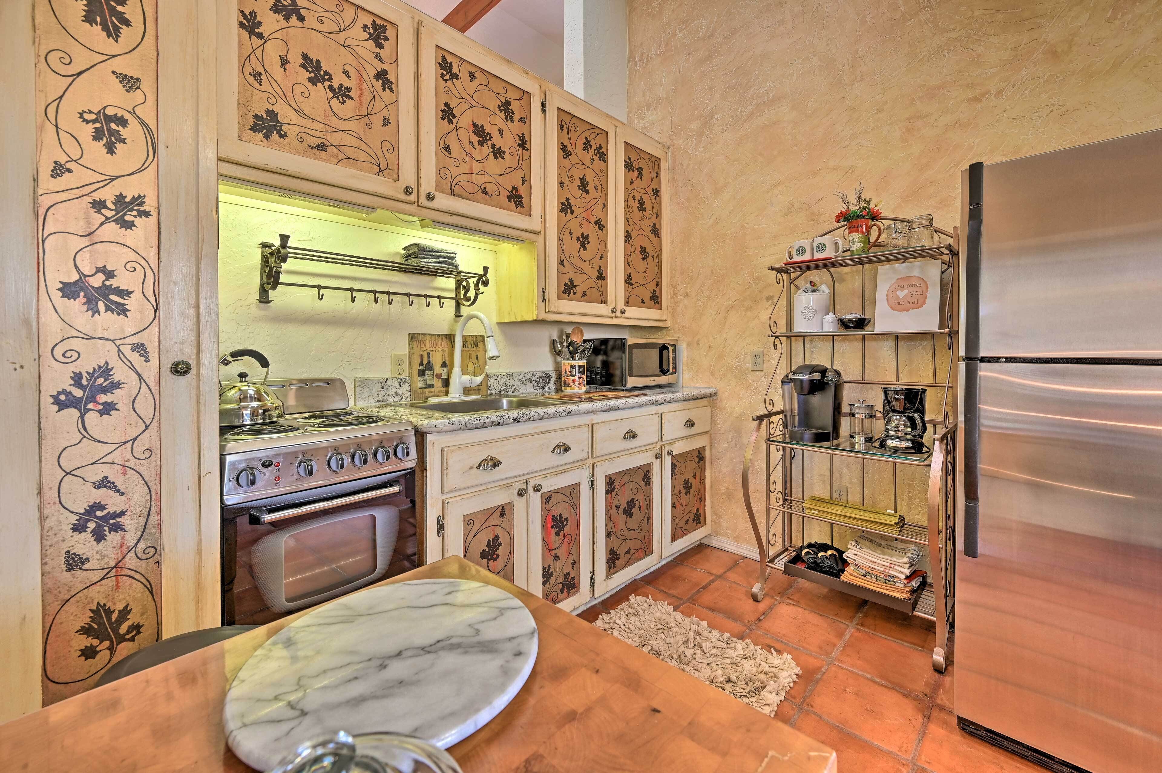 Una cocina con un refrigerador de acero inoxidable, una estufa y un microondas. Hay una mesa de madera con cubierta de mármol y un vaso.