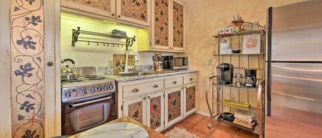 Una cocina con un refrigerador de acero inoxidable, una estufa y un microondas. Hay una mesa de madera con cubierta de mármol y un vaso.