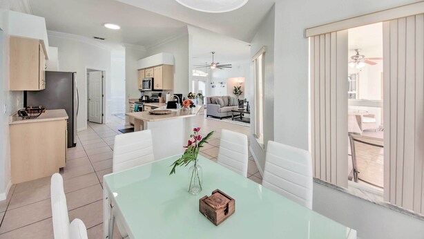 Amplia sala de estar con mesa de comedor, sillas blancas y una cocina al fondo.