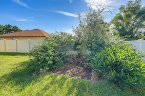 A residential backyard with a paved patio, a variety of shrubs, and a white fence.