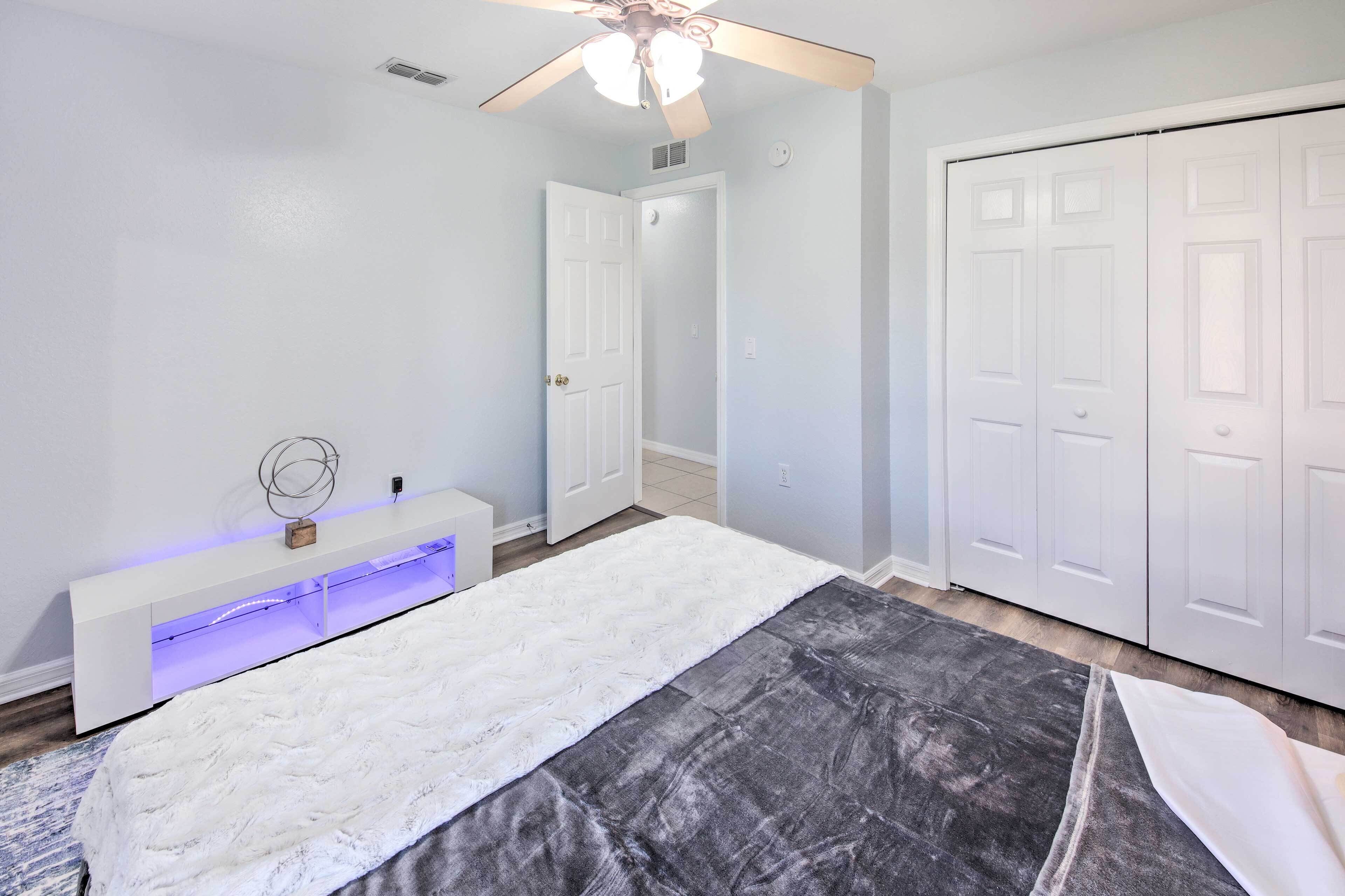 Une chambre à coucher comprenant un lit, un ventilateur de plafond, une console blanche avec une lampe et un placard.