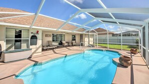 Una piscina exterior cubierta con zona de patio, área de estar techada y vista a un barrio residencial.