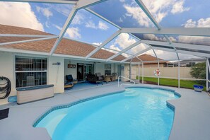 A swimming pool with a covered patio area, outdoor furniture, and a clear sky.