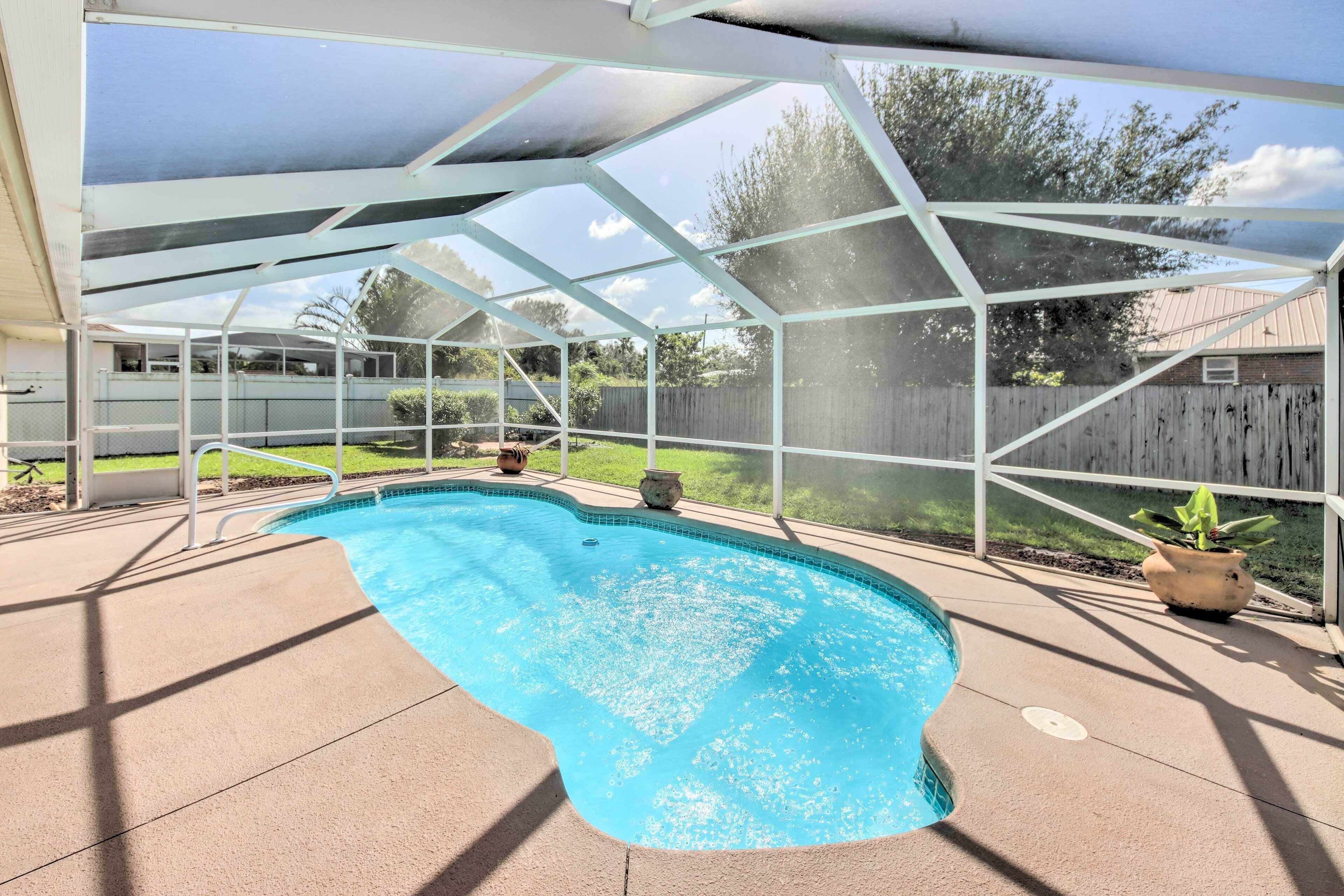 A covered swimming pool with a clear view of the backyard, including a wooden fence and potted plants.