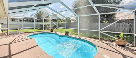 A covered swimming pool with a clear view of the backyard, including a wooden fence and potted plants.