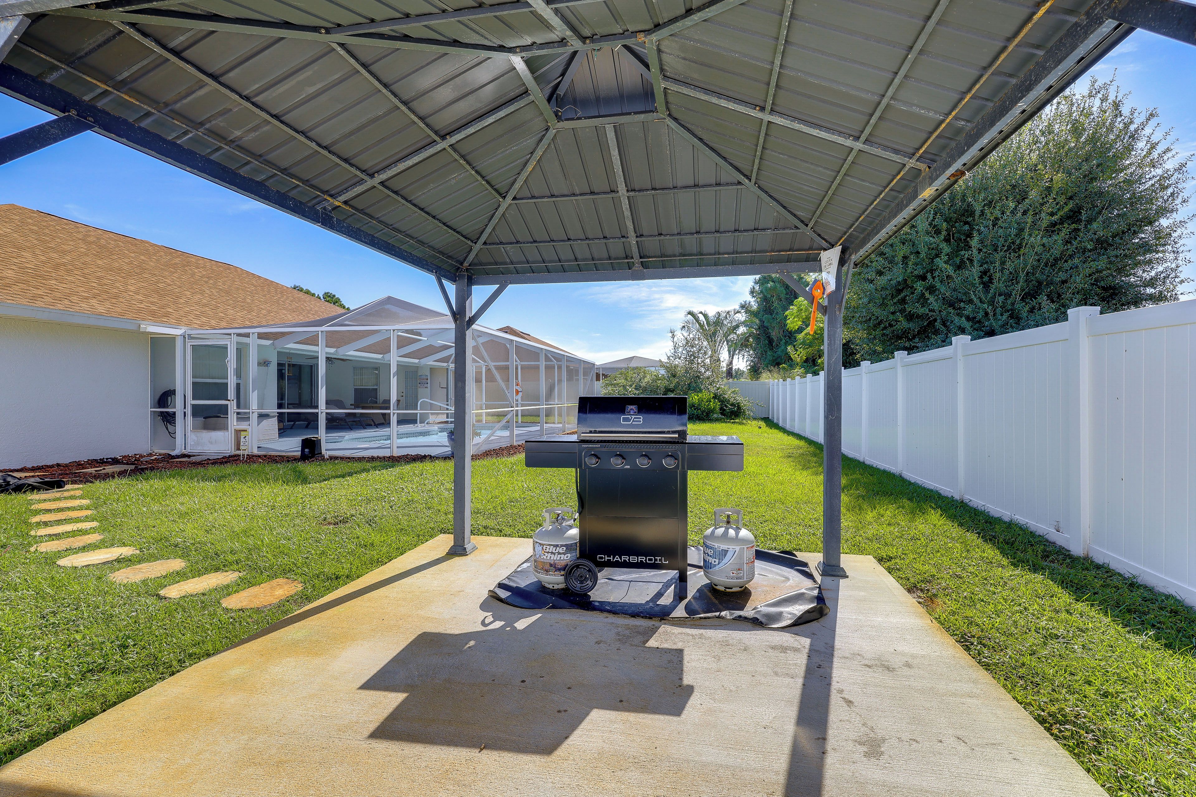 A covered patio area with a barbecue grill, gas cylinders, and a pool in the background.