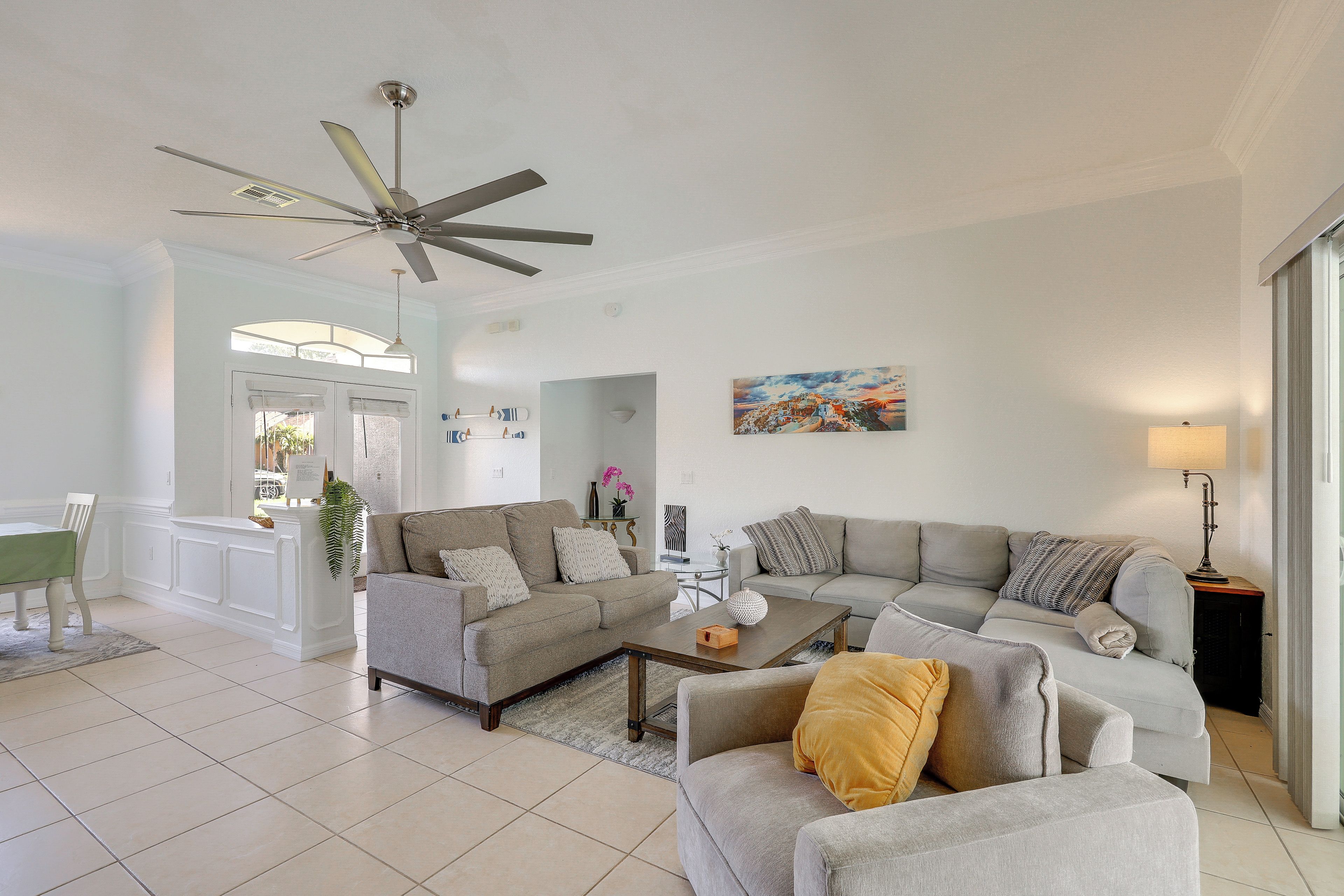 Uma sala de estar ampla com ventilador de teto, área de jantar com mesa e cadeiras, e um quadro na parede.