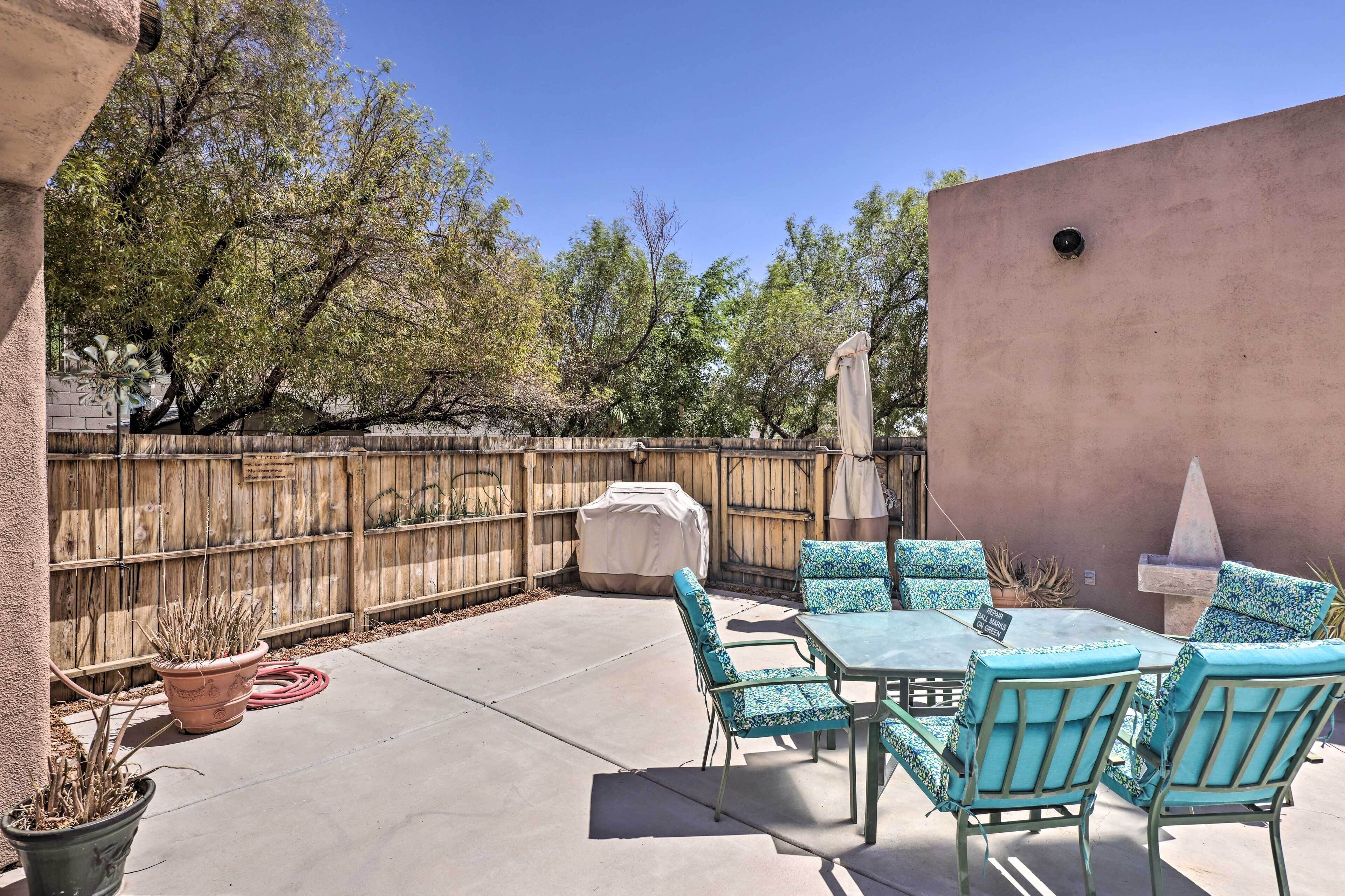 A patio with a table and chairs, a barbecue grill, and potted plants.