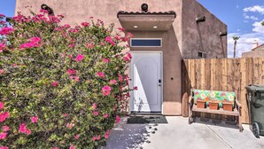 A building with a white door, a wooden bench with potted plants, and a wooden fence.