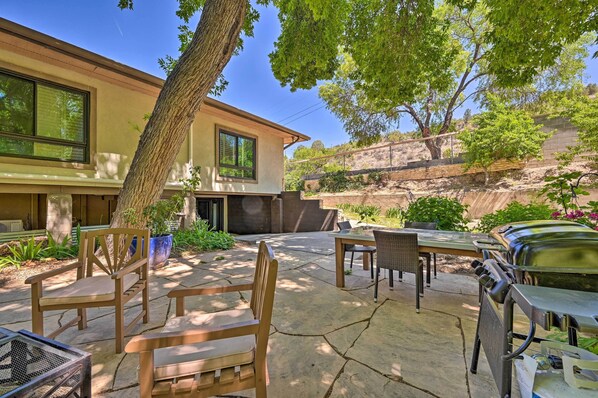 Une terrasse avec des meubles d’extérieur, un barbecue et une maison dotée de grandes fenêtres.