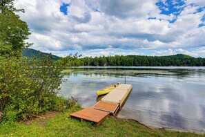 A calm lake with a wooden dock extending into the water, surrounded by lush greenery and a forested hill in the background. - Rustic Adirondacks Home w/ Hot Tub & Lake Access! (Chestertown)