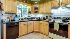 A kitchen with wooden cabinets, a dishwasher, a stove, and a window with a view of trees. - Rustic Adirondacks Home w/ Hot Tub & Lake Access! (Chestertown)