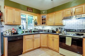 A kitchen with wooden cabinets, a dishwasher, a stove, and a window with a view of trees. - Rustic Adirondacks Home w/ Hot Tub & Lake Access! (Chestertown)