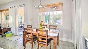 A dining area with a wooden table and chairs, a hanging light fixture, and a window with a view of greenery. - Spacious Palm Desert Retreat w/ Outdoor Oasis! (Palm Desert)