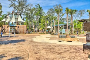 Un espace de jeux avec une structure ludique sur le thème des pirates, entouré d’arbres et bordé d’un bâtiment doté d’un toit végétalisé.