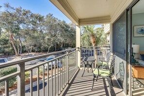 Un balcon avec une table et des chaises, une vue sur les voitures garées et les arbres, et un bâtiment doté d’une fenêtre et d’œuvres d’art.