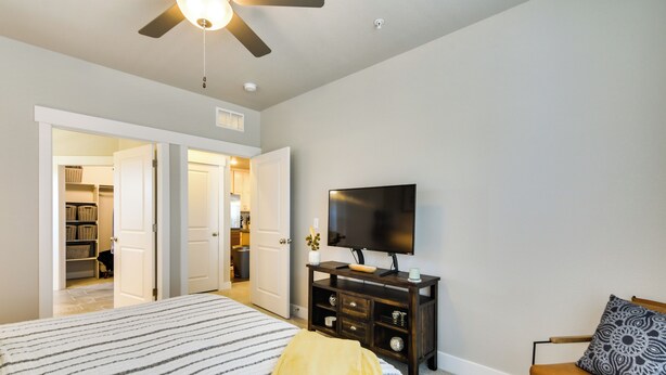 A bedroom with a bed, a TV, a ceiling fan, and a wardrobe. - Elegant Loveland Condo < 5 Mi to Old Town! (Loveland)