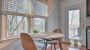 Ein Essbereich mit Tisch und Stühlen, ein Fenster mit Jalousien und Blick auf Bäume.