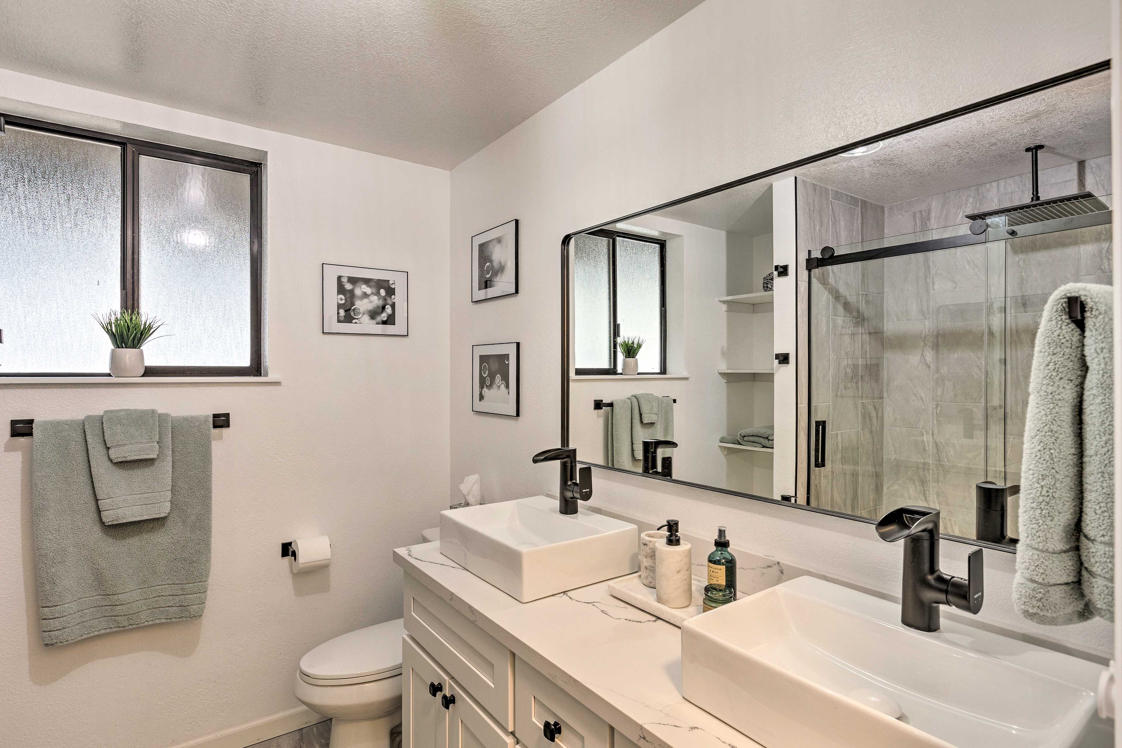 Un baño moderno con dos lavabos, inodoro, un espejo grande y cabina de ducha de vidrio.