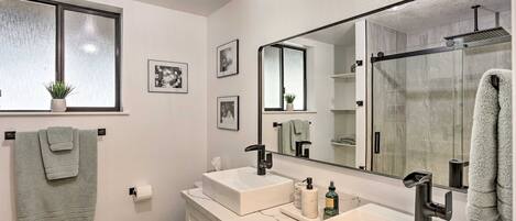 Un baño moderno con dos lavabos, inodoro, un espejo grande y cabina de ducha de vidrio.