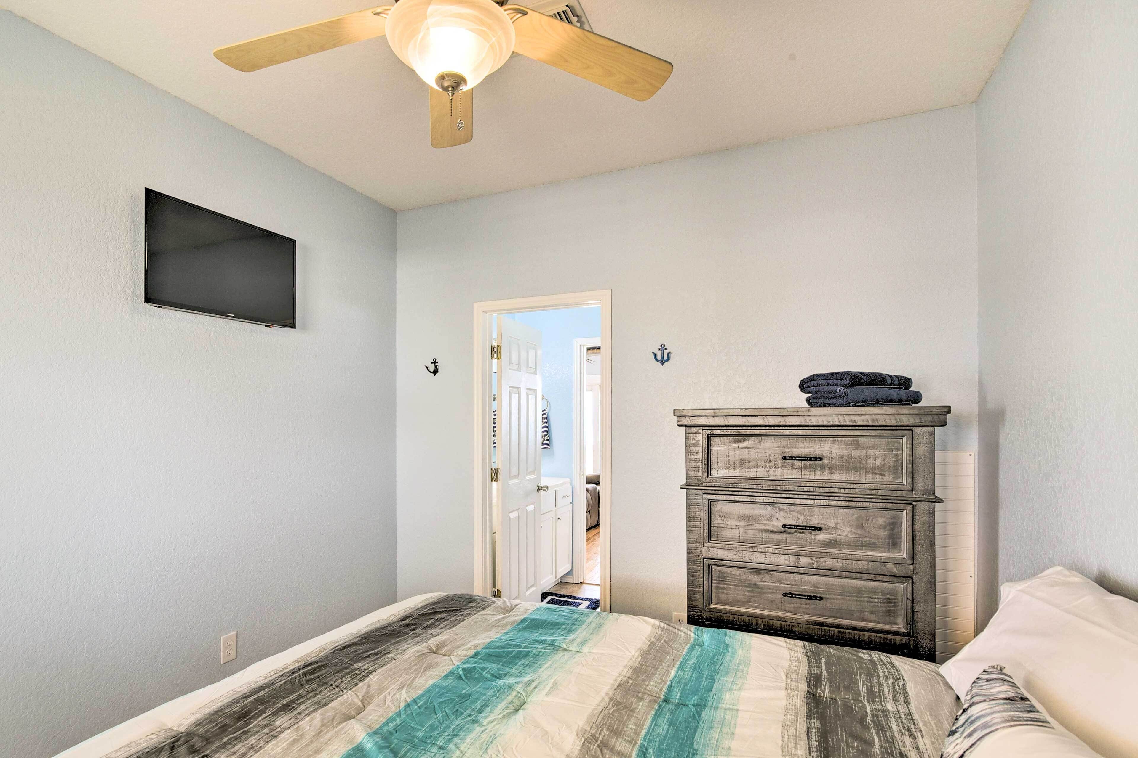 A bedroom with a bed, a dresser, a ceiling fan, and a TV mounted on the wall.