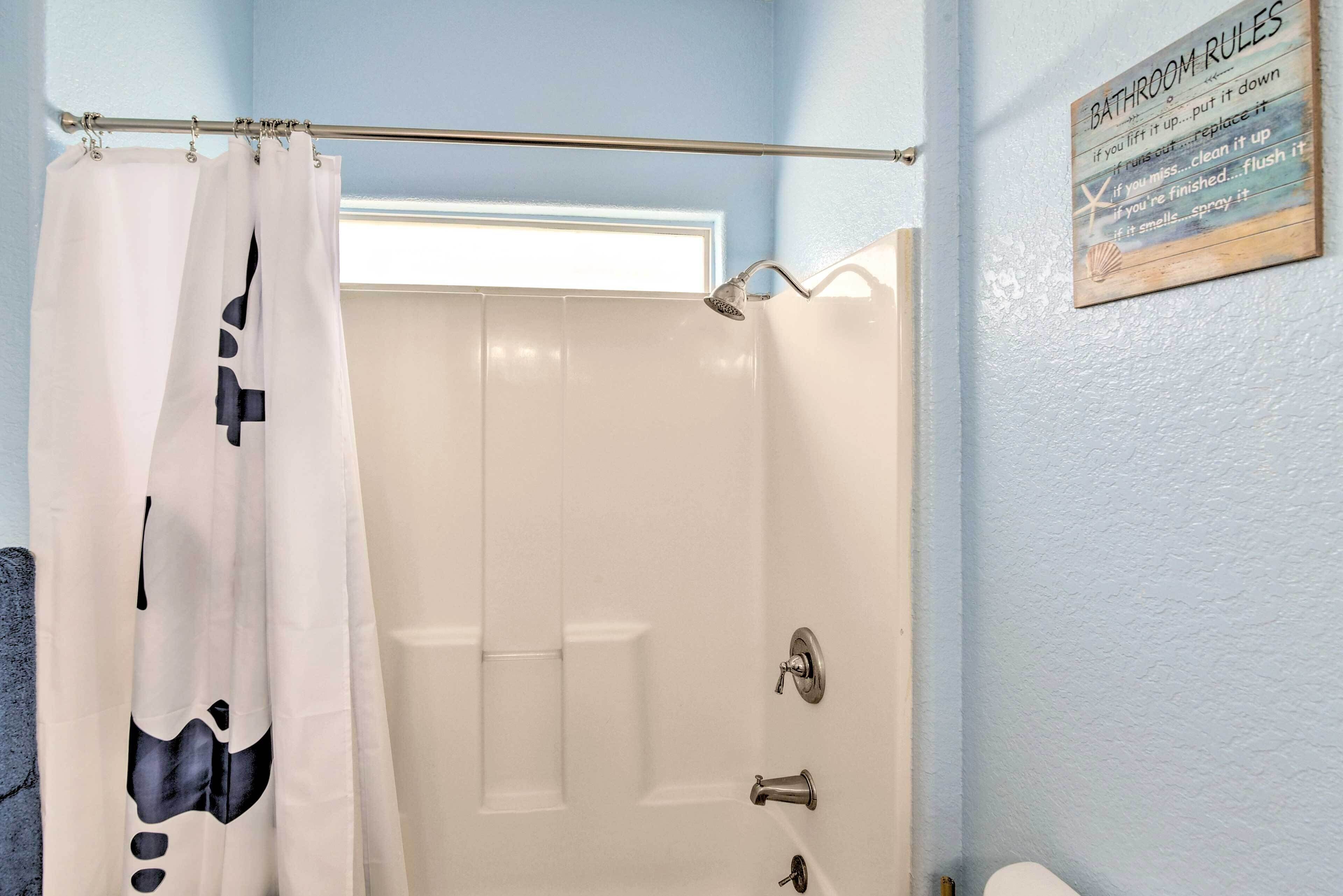 A bathroom with a shower curtain featuring a black and white abstract design, a showerhead, and a sign with bathroom rules.