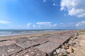 A rocky shoreline with a clear view of the ocean and a distant pier.