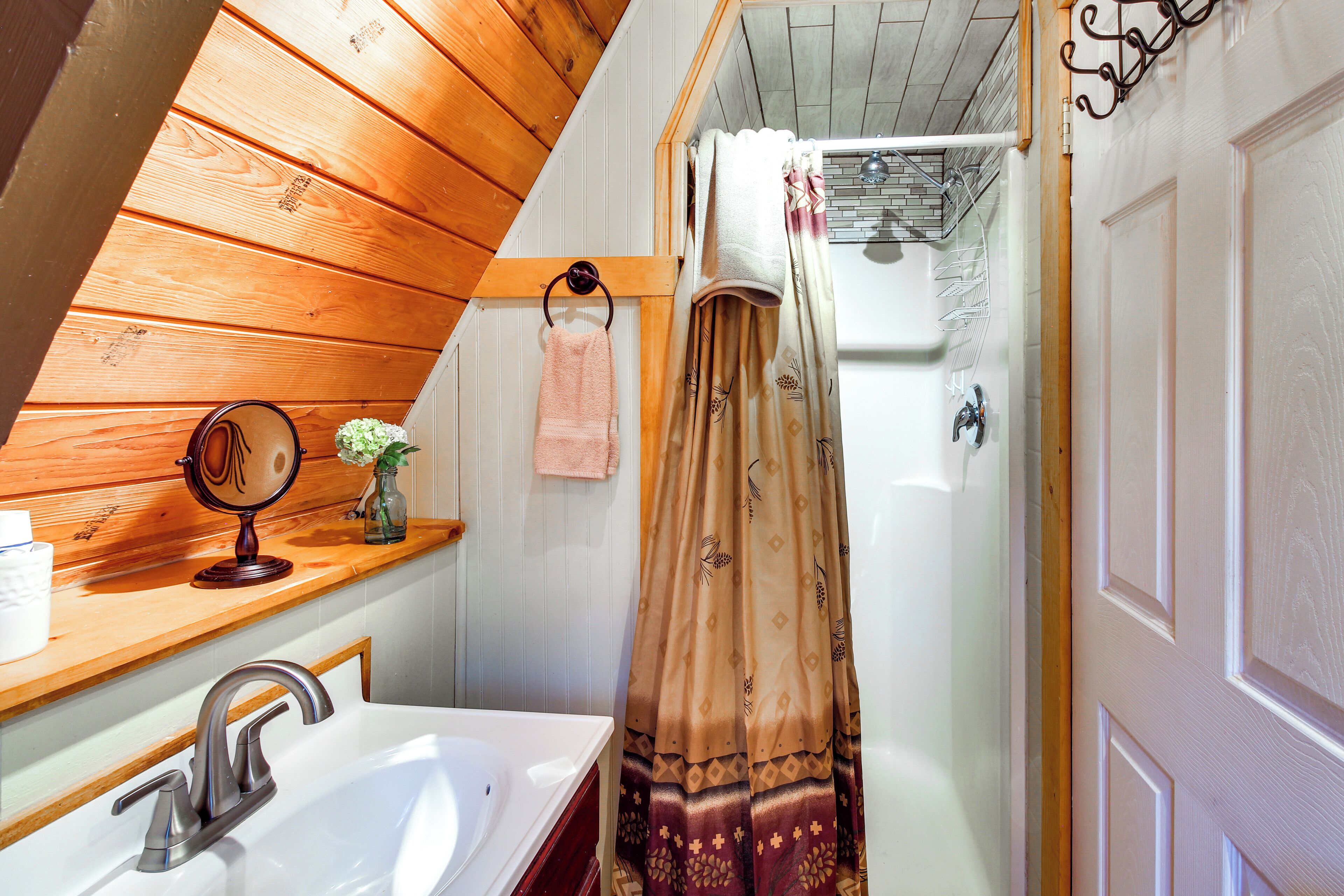 Ein Badezimmer mit Holzbalkendecke, einem weißen Waschbecken, einem Spiegel und einer Duschvorhang.
