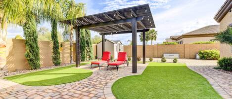 Un patio con pérgola, sillas reclinables rojas y un césped cuidado.