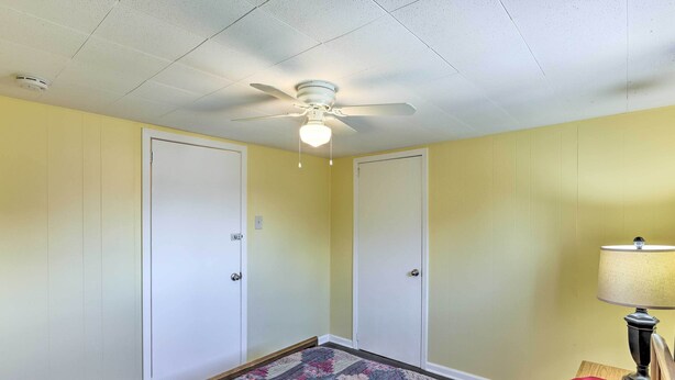 A room with a ceiling fan, two white doors, a patterned carpet, and a lamp on a nightstand. - Lovely Milwaukee Getaway - Family Friendly! (Milwaukee)