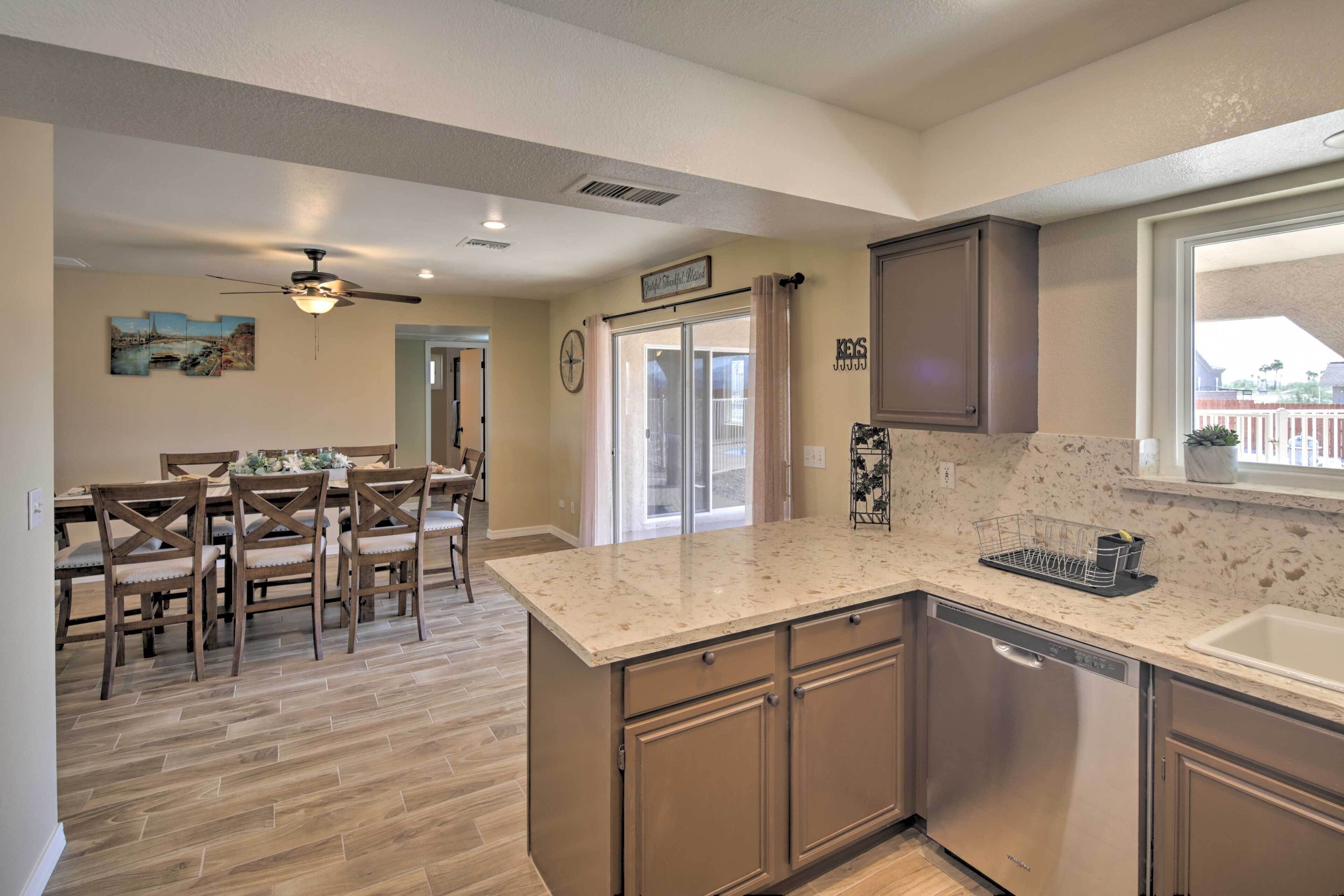 A kitchen with a dishwasher, a dining area with wooden chairs, and a ceiling fan.